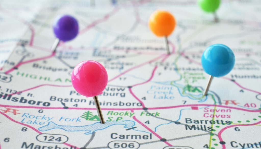 Colorful pushpins thumbtacks pins in a map with blurry background. Travel trip concept.