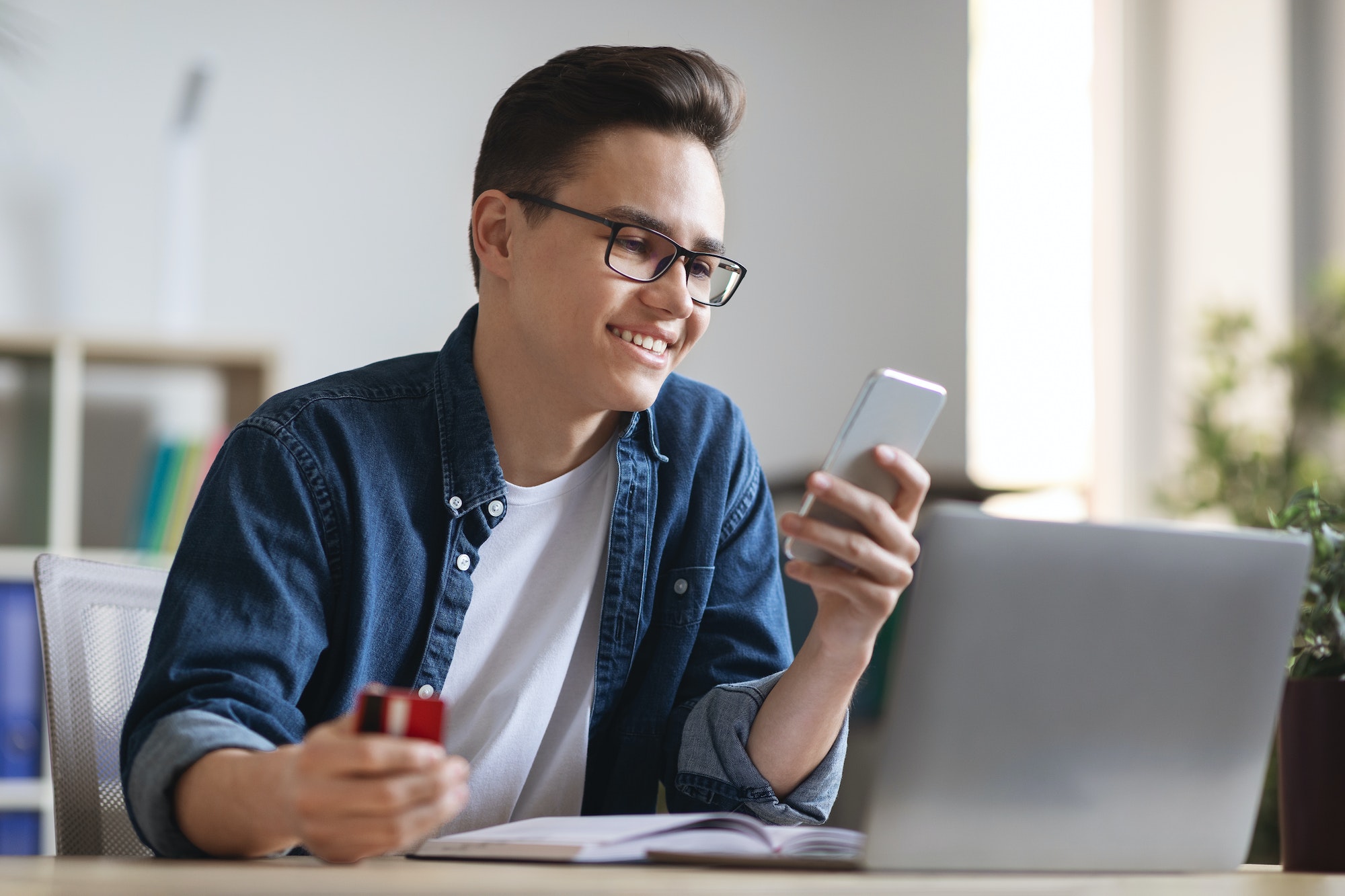 Smiling Young Office Worker Holding Credit Card And Smartphone, Making Order Online